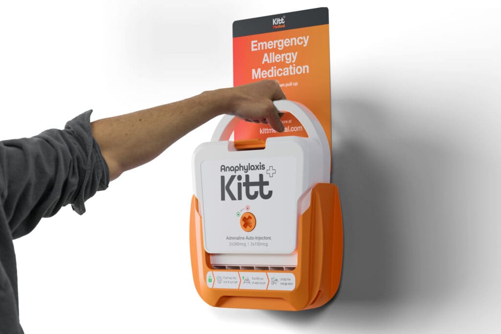 The wall-mounted Anaphylaxis Kitt being lifted from its bracket — emergency allergy medication, ready on the wall